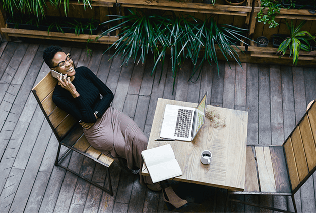 A woman sitting on a patio with her laptop and phone, setting up a professional email