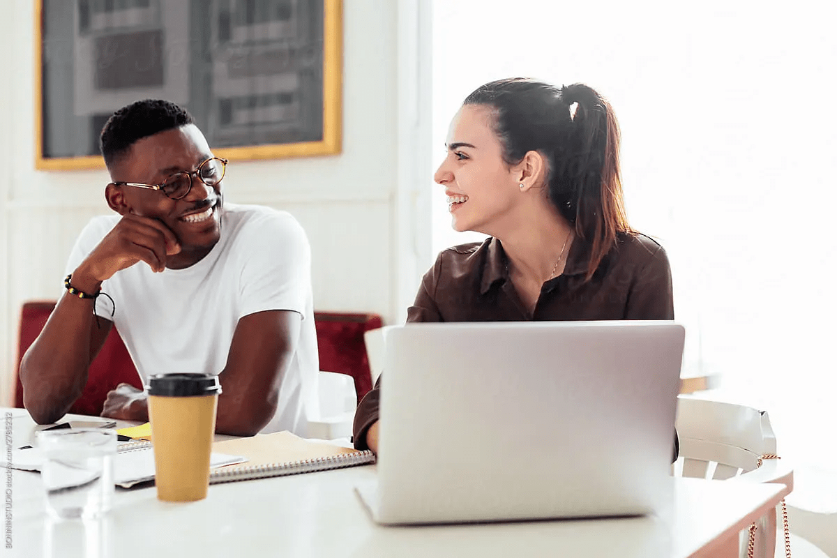 Two people on laptops looking at each other smiling