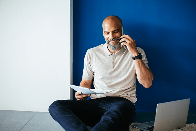 man sitting on floor talking on the floor with documents in his hands