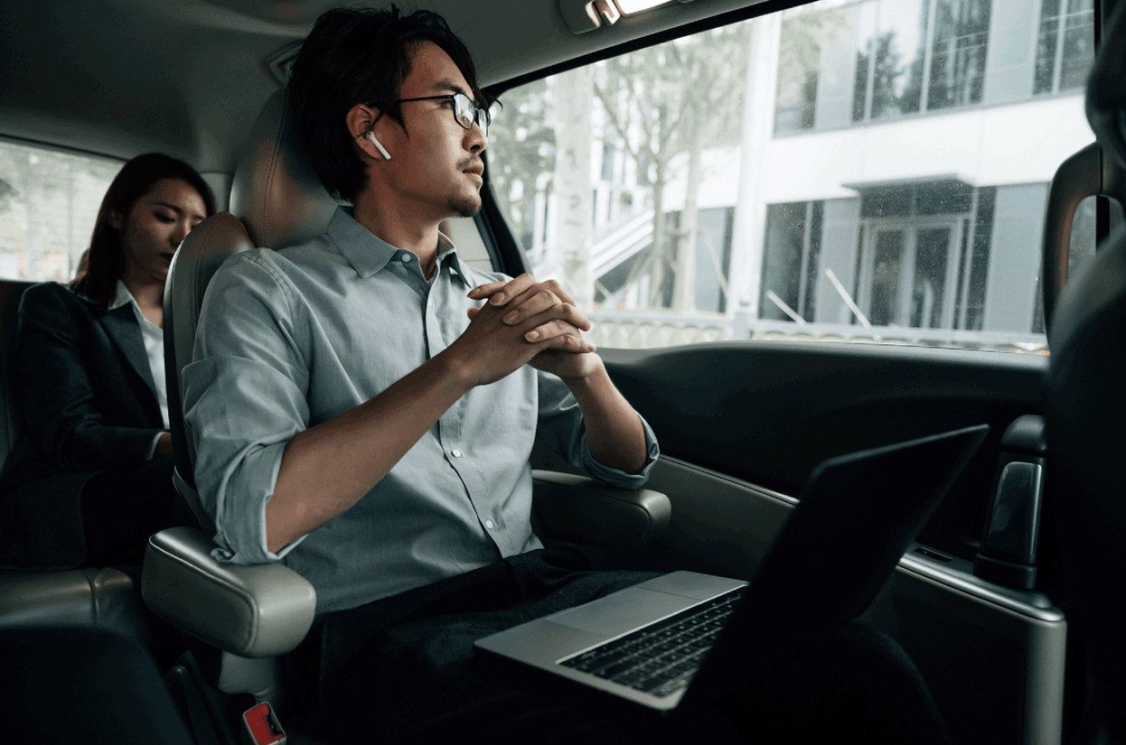 Man working on his laptop inside of a driving car 