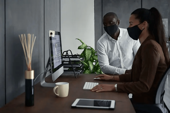 Two people looking at a laptop wearing masks