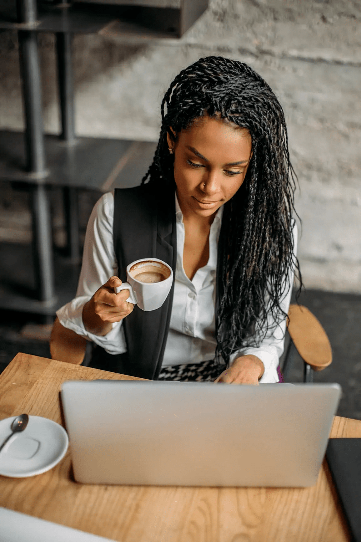 woman looking at her laptop while holding coffee